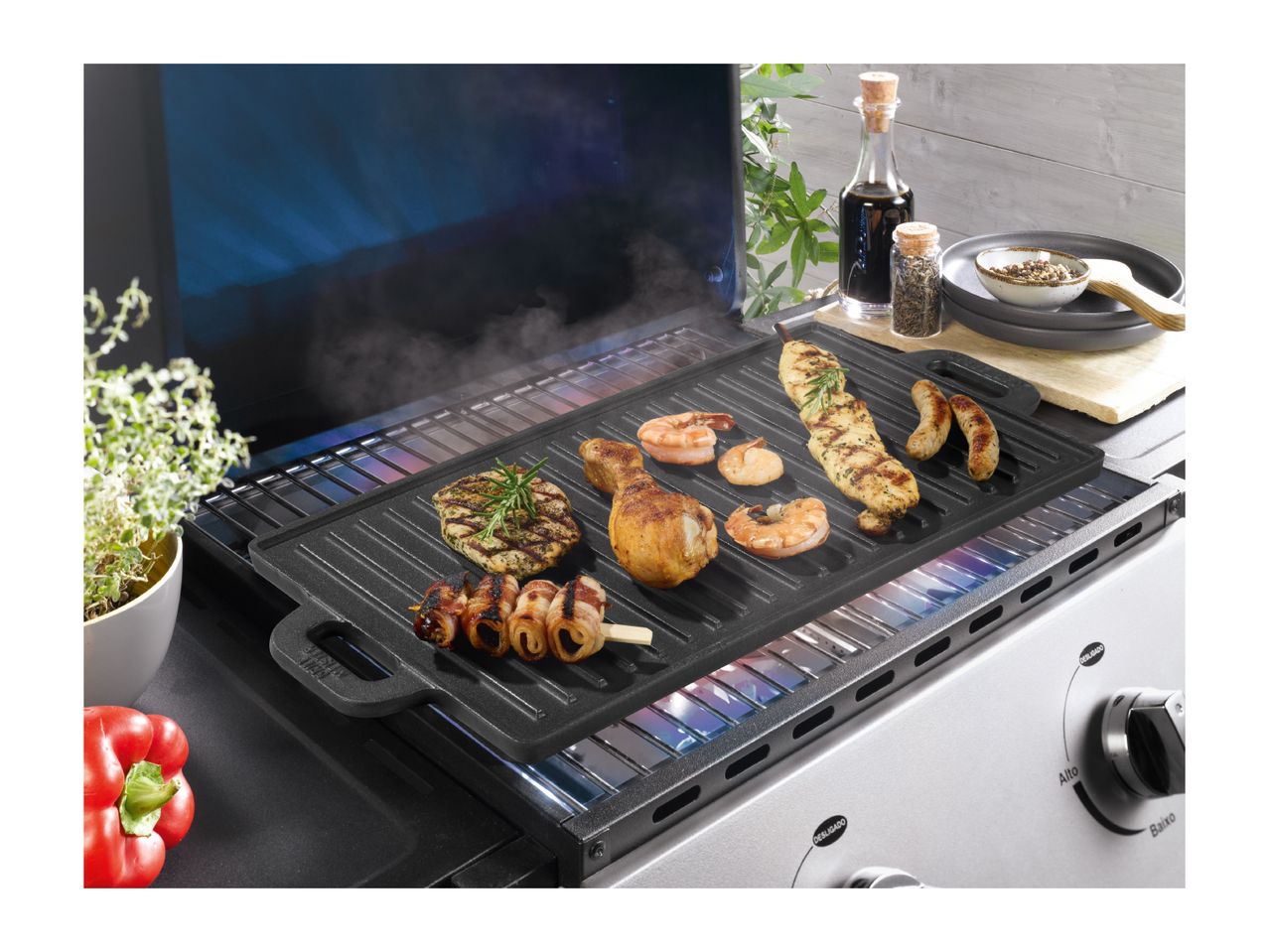 Grill with various meats and shrimp cooking, with spices and a red pepper nearby.
