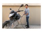 Man pressure washing a motorcycle in front of a modern building.