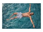 Man in striped swim shorts floating on his back in clear blue water.