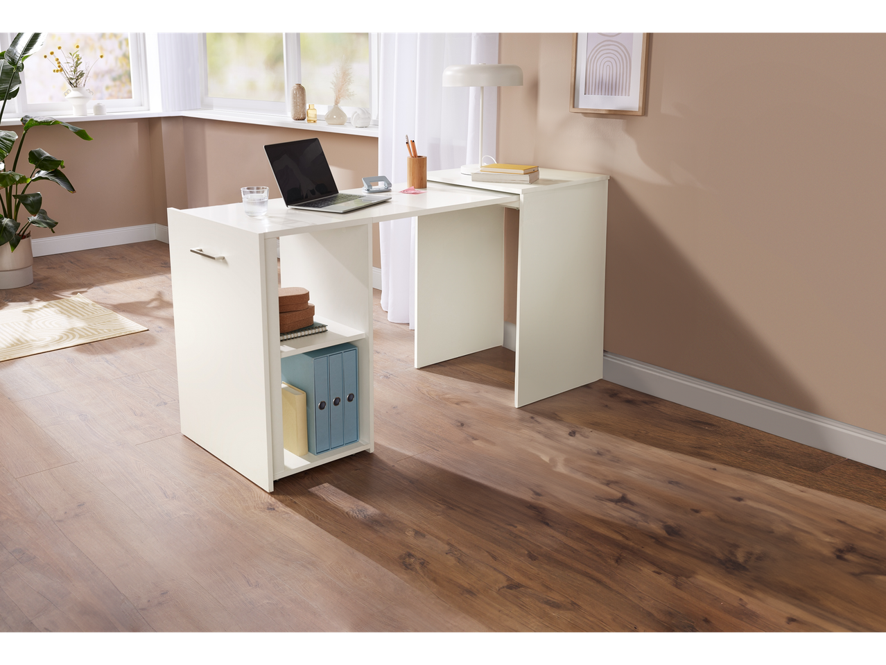 Ein weißer L-förmiger Computertisch mit eingebauten Regalen steht in einem hellen Raum.