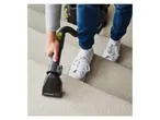 A person using a Hurricane Cat 2 vacuum cleaner attachment on carpeted stairs.