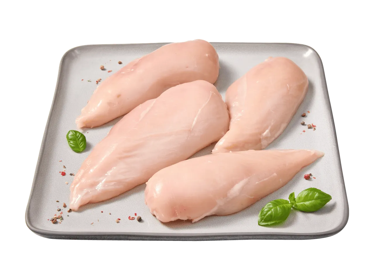 Quatre filets de poulet crus sur une assiette grise, garnis de basilic et de grains de poivre.
