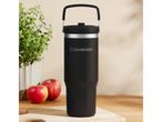 Black SilverCrest travel mug with handle, apples, and a plant on a wooden surface.