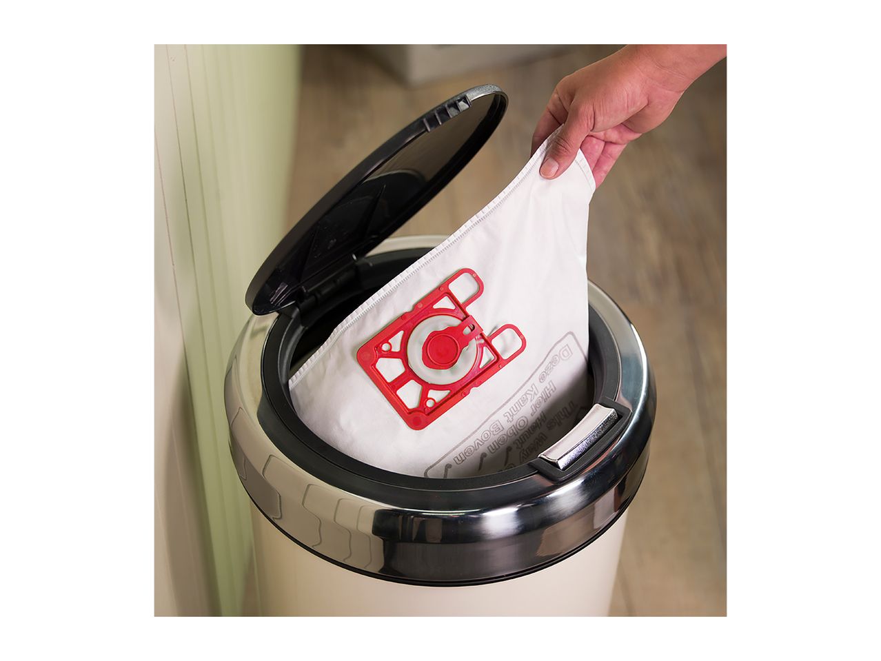 A hand disposes of a used vacuum cleaner bag into a bin.