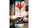 A person uses a drill press to bore a hole in a piece of wood secured in a vise.