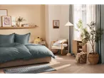 Quarto luminoso com cama, roupa de cama azul-acinzentada e decoração moderna.