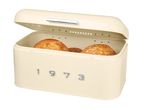 Retro cream-colored metal bread bin with the year 1973 on the front, containing bread rolls