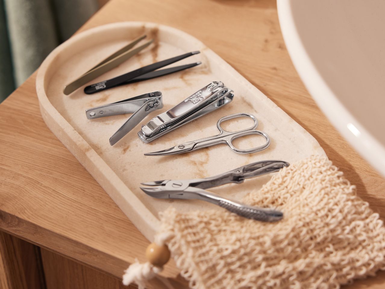 Manicure set with nail clippers, scissors, and tweezers on a tray next to a loofah.