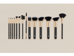 A collection of black and gold makeup brushes of various sizes and shapes, neatly arranged on a light background.