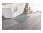 A light green bath mat on a gray tiled floor next to a white bathtub with a towel.