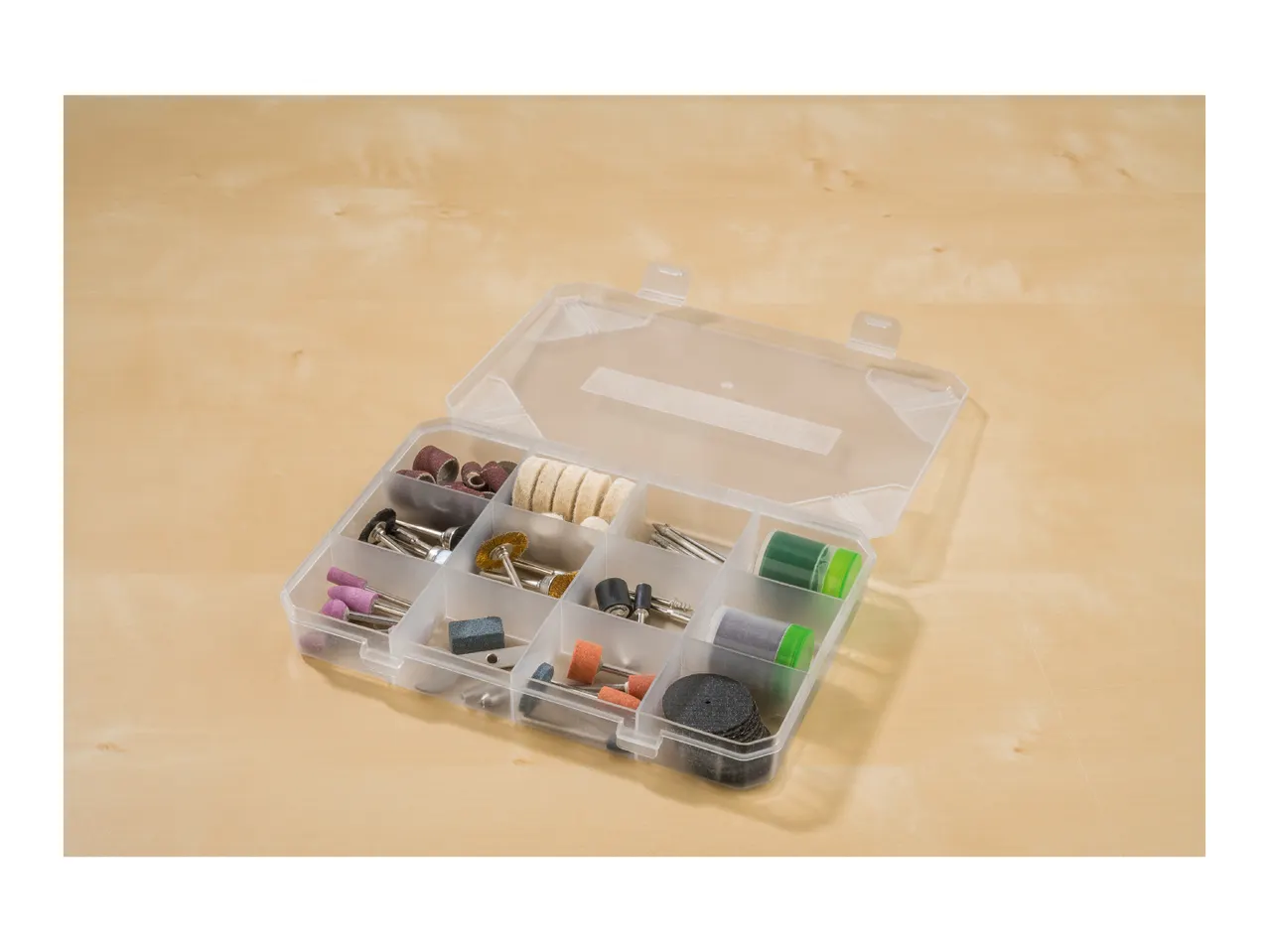 A clear plastic organizer box filled with various rotary tool accessories on a light wooden surface.