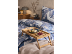 A bamboo breakfast tray holds a plate of food and grapes on a bed with blue and white bedding.