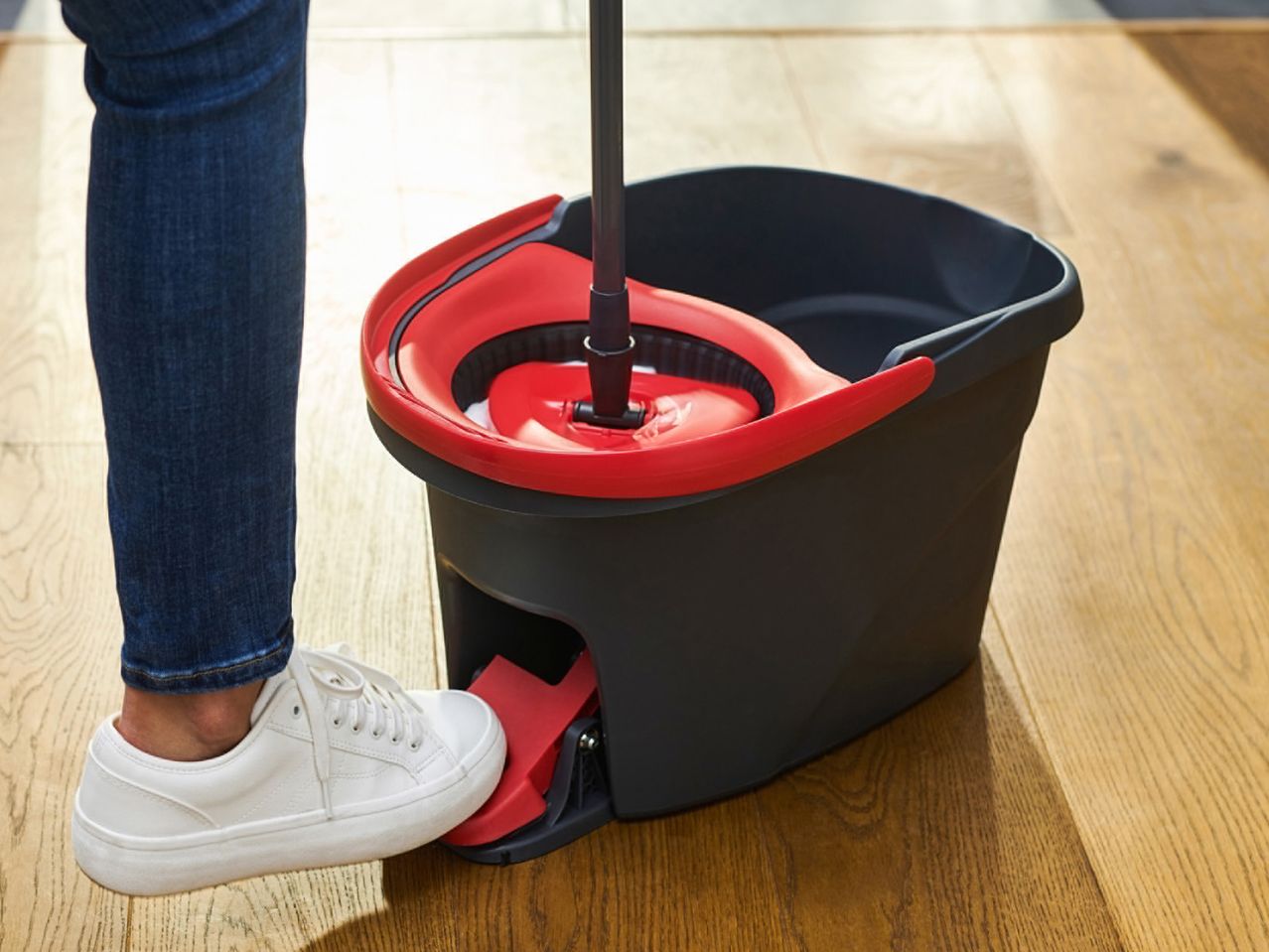 A person uses a spin mop and bucket to clean a hardwood floor.