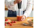Persoon blendt tomatensoep met een staafmixer, omringd door verse tomaten.