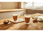 Trei pahare de latte pe o masă din lemn, cu macarons și zahăr.