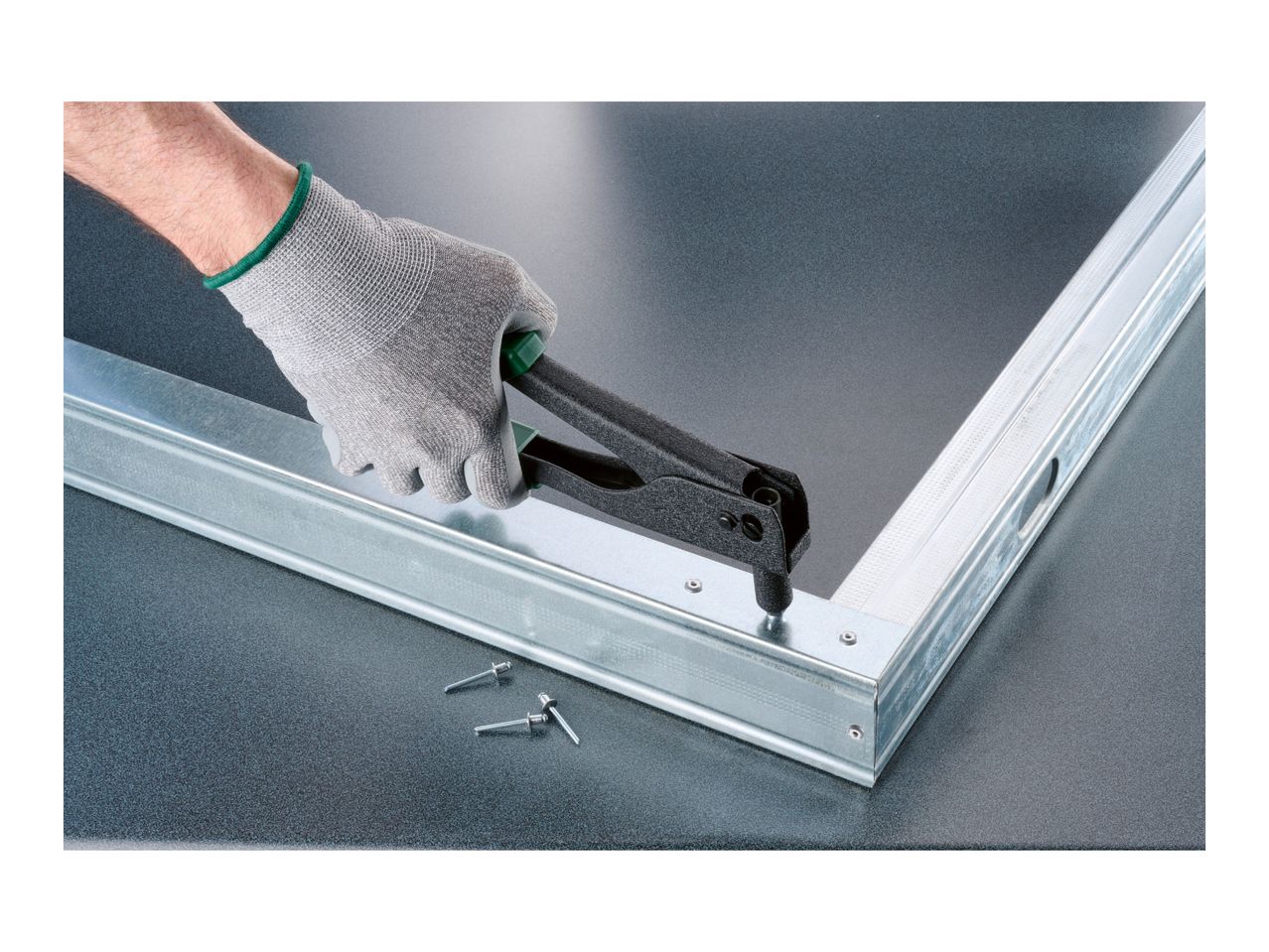 Hand in work glove using a rivet gun to fasten metal profiles.