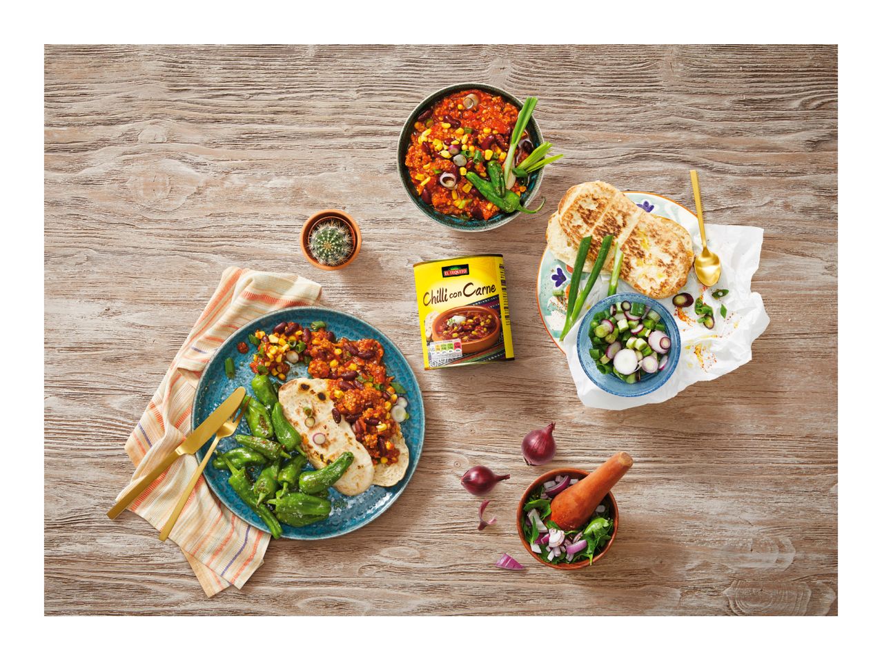Chilli con carne with flatbread, green peppers, and fresh ingredients on a wooden table.