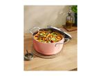 Pink cooking pot filled with pasta, meat sauce, and green onions on a wooden table.