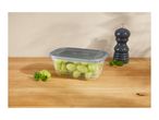 A clear plastic container filled with green grapes on a wooden surface next to a dark gray pepper mill.