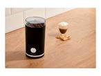 Coffee grinder with coffee beans, a glass of coffee, and cookies on a wooden counter.