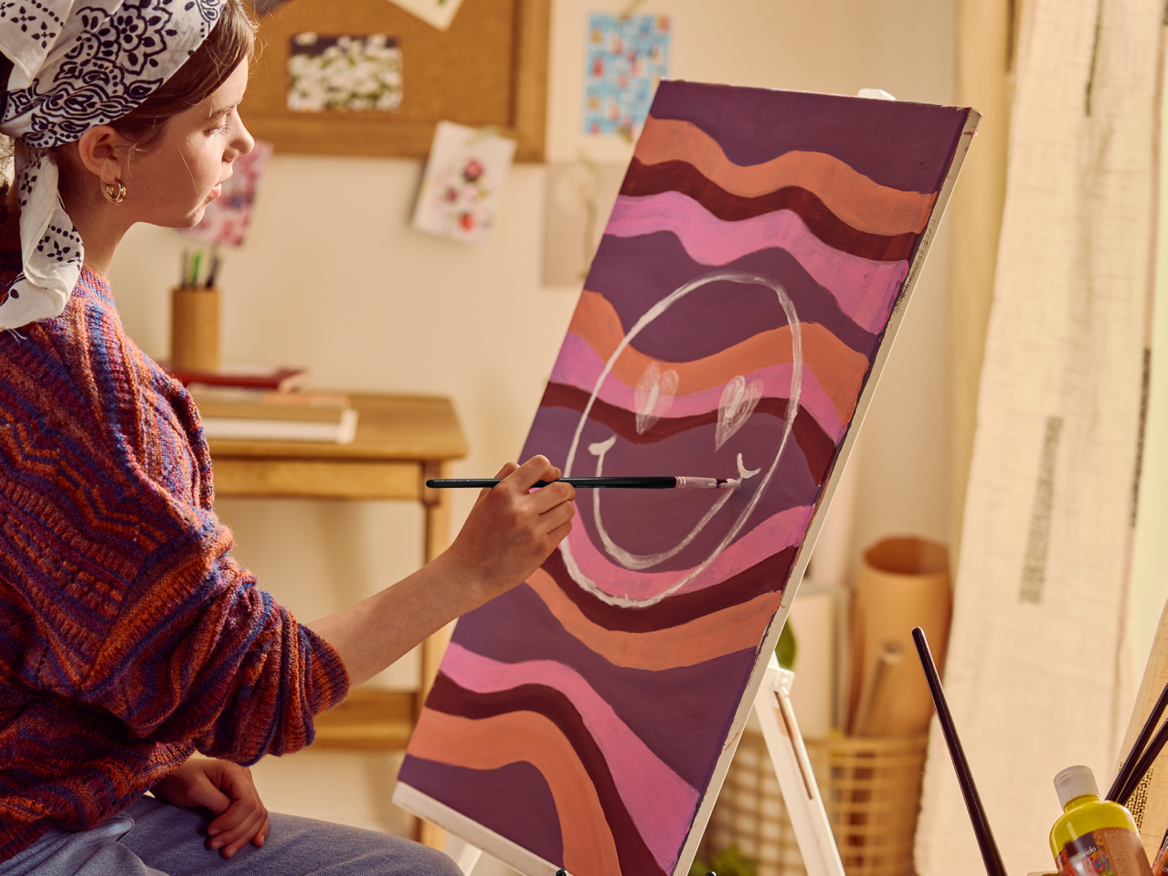 Млада жена рисува усмихнато лице върху платно с вълнообразни шарки.