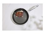 A stainless steel frying pan with a honeycomb pattern, containing a cooked steak, onions, and herbs.