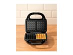 Open waffle maker with one cooked waffle and empty waffle plates on a wooden surface.