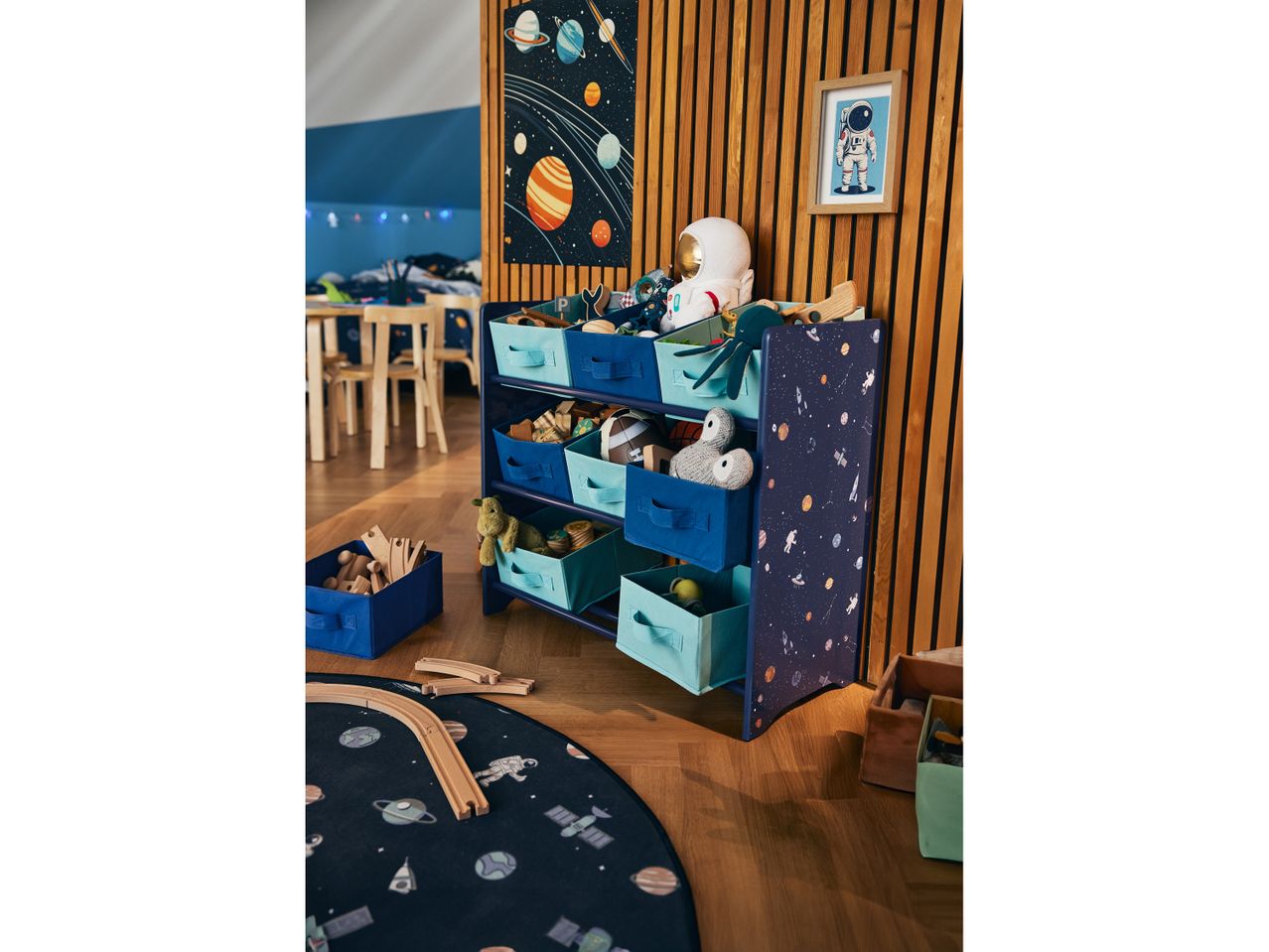 A child's navy blue and teal space-themed storage unit with fabric bins, filled with toys, sits in a playroom.