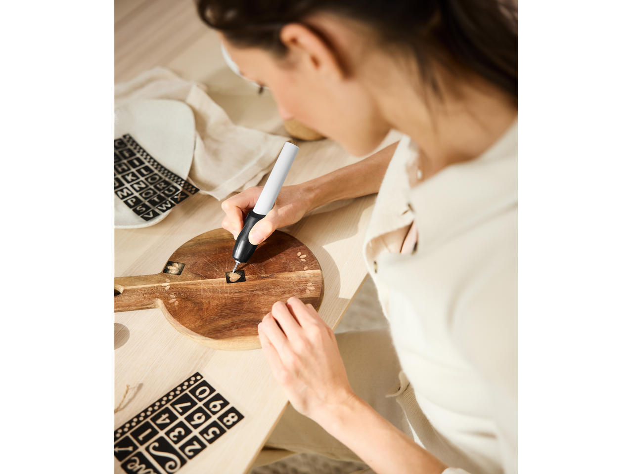 Crelando® Gravierstift, der von einer Frau zum Gravieren eines Holzbretts mit Buchstaben verwendet wird.