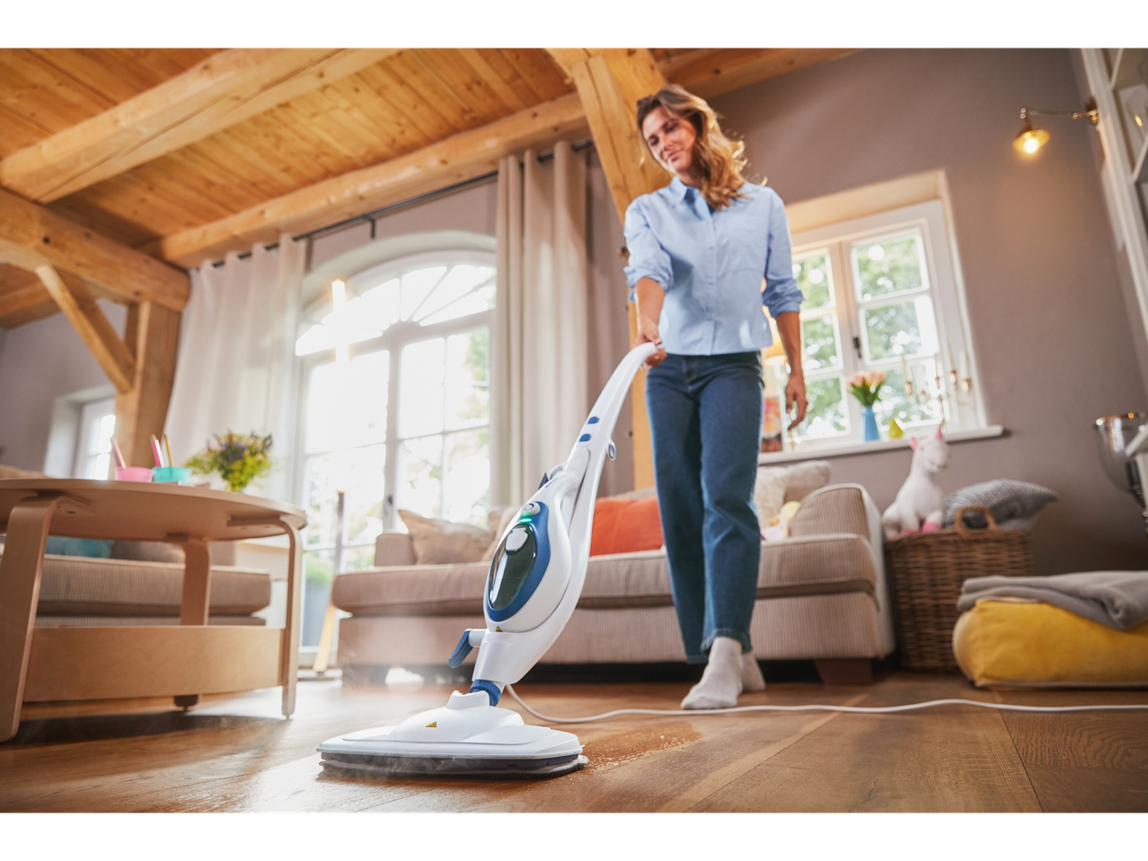 Uma mulher usa um mop a vapor para limpar um piso de madeira.