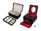 To sorte smykkeskrin, et rektangulært med beige interiør og et ovalt med rødt interiør og spejl.