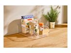Clear storage box with pasta, lentils, and spices on a wooden counter next to a plant.