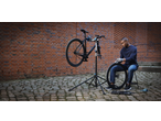 Man repairing a bicycle on a repair stand, holding a wheel, with tools nearby.