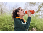Woman drinking from an orange CRIVIT drink bottle outdoors.