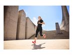 Woman running in black activewear and orange running shoes on concrete steps.