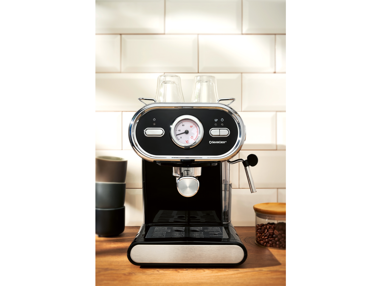 Máquina de café preta com medidor de temperatura e chávenas numa bancada de madeira.