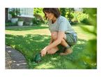 Woman trimming grass edges with a handheld grass shear in a garden.