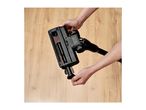 Hands attaching a brush head to a black vacuum cleaner on a wooden floor.