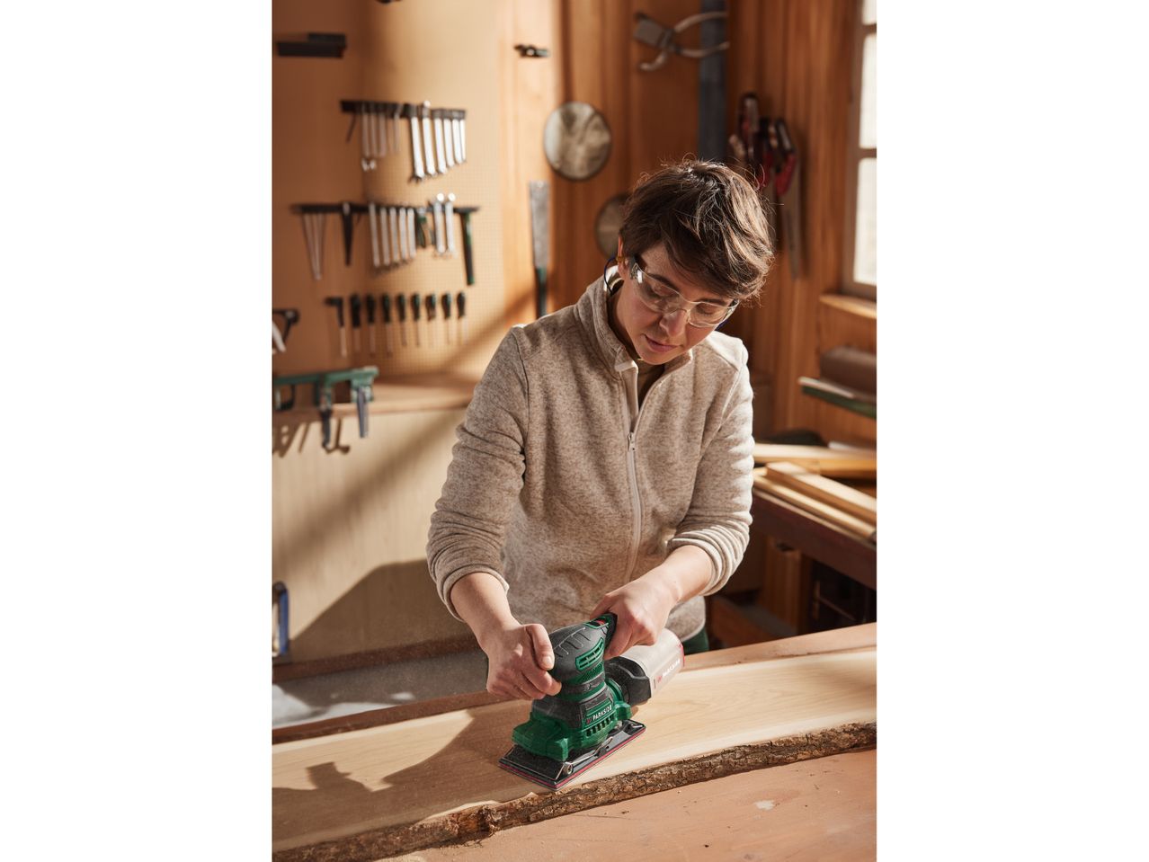 A woman uses a Parkside electric sander on a piece of wood in a workshop.