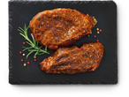 Kaks marineeritud lihatükki rosmariini ja piprateradega mustal kiltkiviplaadil.