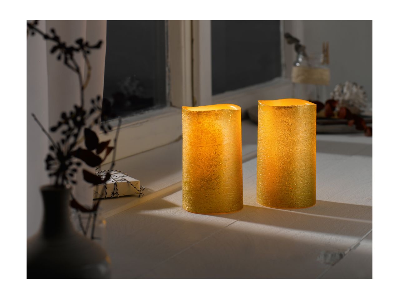 Two glowing LED candles on a windowsill at night, with a dark window in the background.