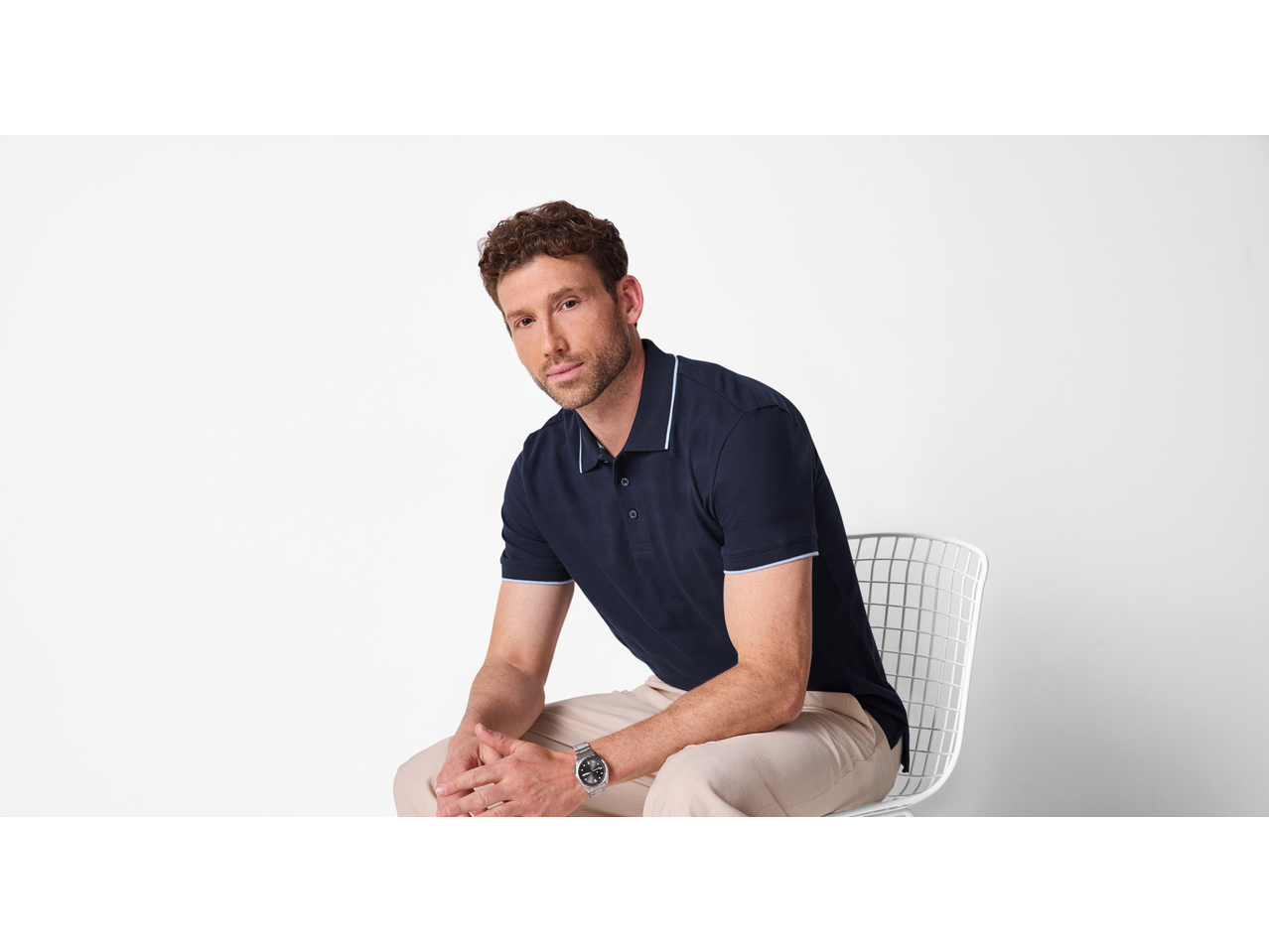 Férfi sötétkék ESMARA MEN pólóingben és bézs nadrágban, széken ülve.
