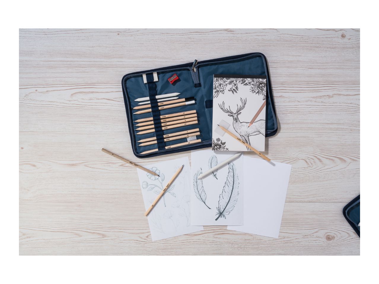An art kit with pencils, paper, and a sharpener on a wooden table.