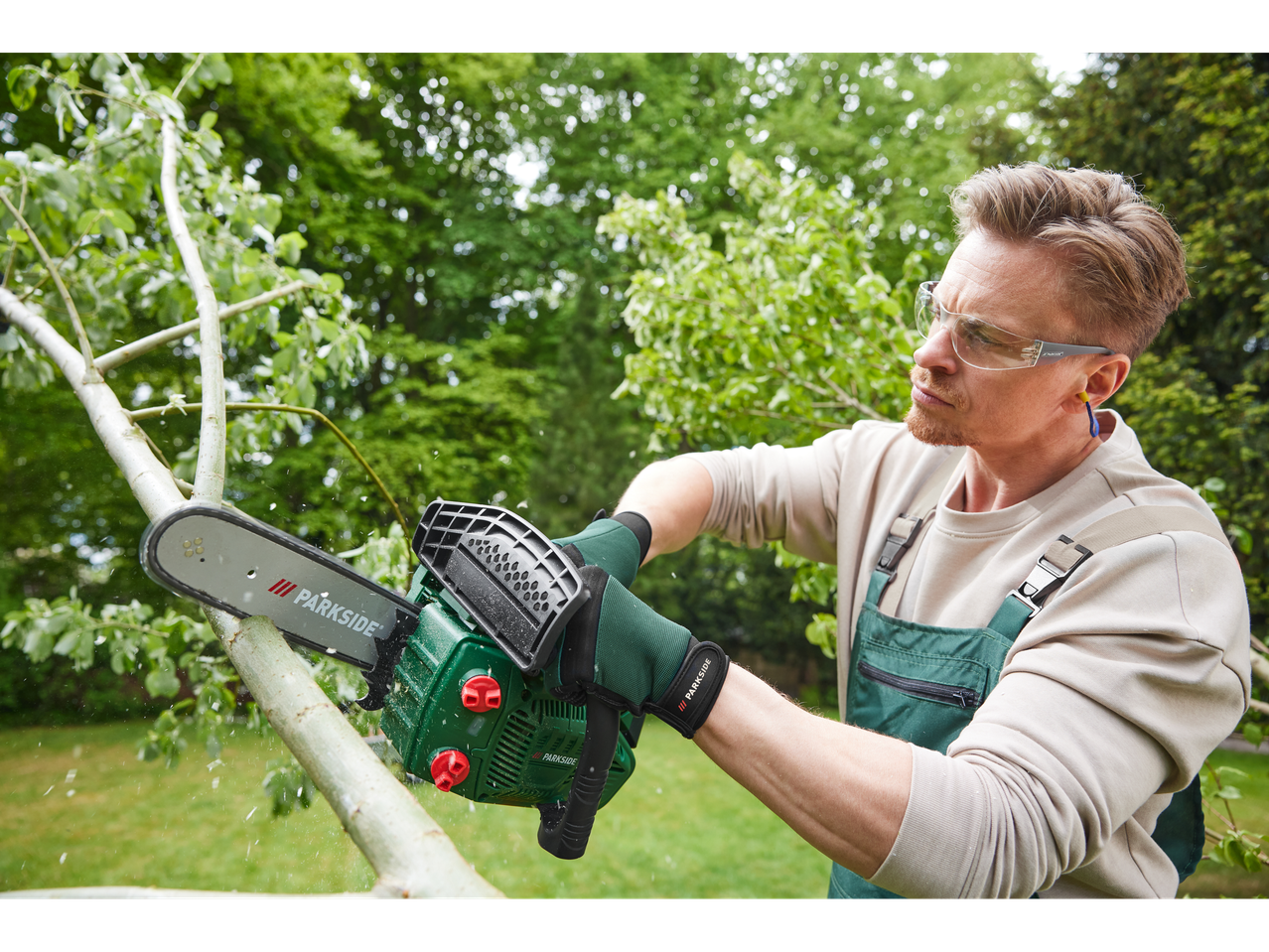 A man uses a Parkside chainsaw to cut a tree branch.