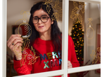 Woman decorating a window with crelando® Markers, drawing Christmas baubles and holly.
