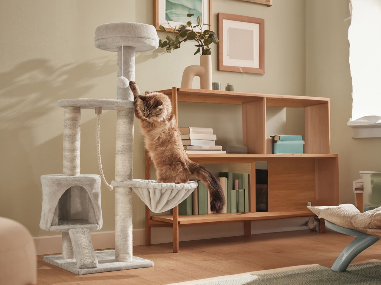 A cat plays on a grey Cat Activity Tower next to a light wood shelf.