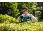 A woman uses a Parkside electric hedge trimmer to trim a hedge in her garden.