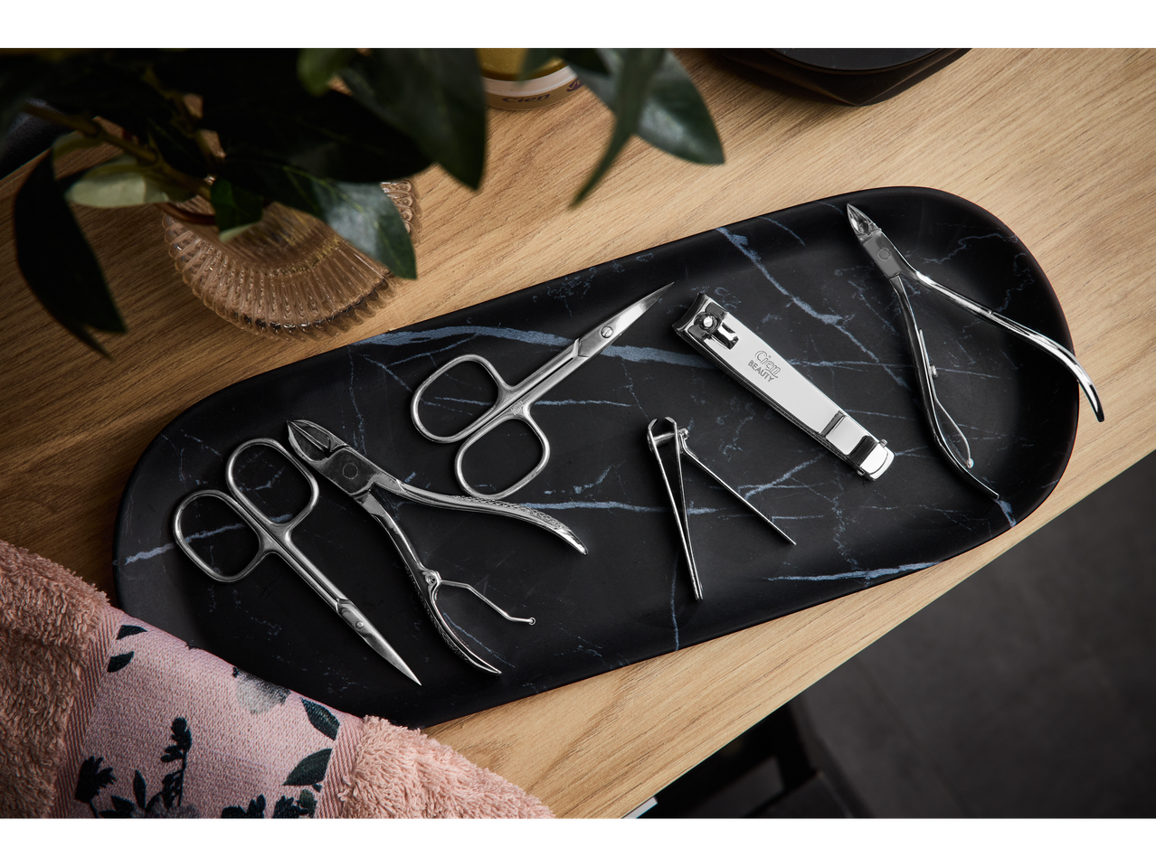 Manicure and pedicure accessories, including nail clippers with 'Cien BEAUTY' branding, on a black marble tray.