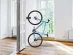 Una bicicletta blu è appesa verticalmente a una parete bianca con un supporto EASYmaxx.