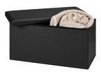 Black storage ottoman with a beige rolled blanket inside, lid slightly ajar.